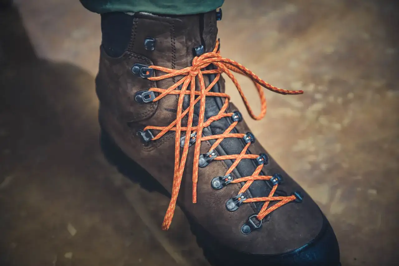 Brązowy but trekkingowy z pomarańczowymi sznurówkami, pokazujący, jak wiązać buty trekkingowe.