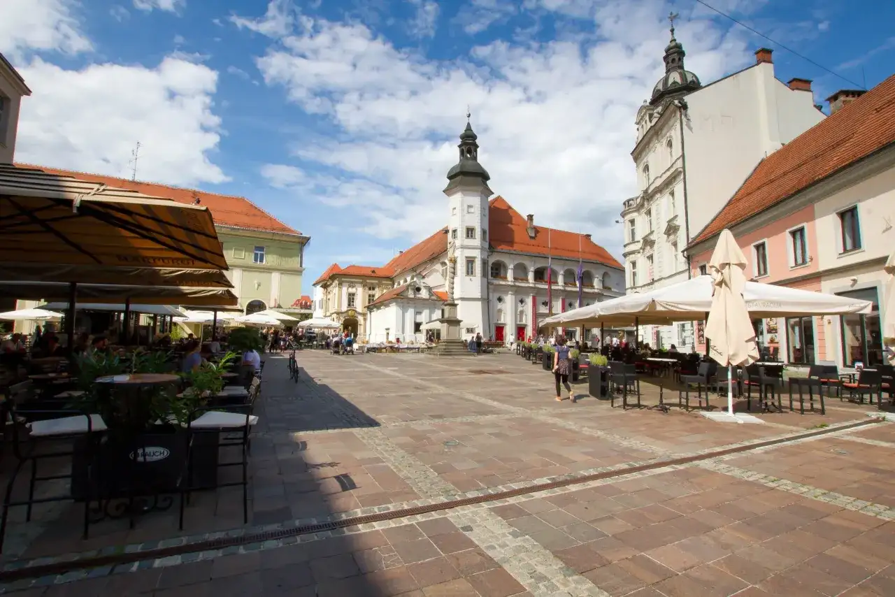 Rynek w Mariborze z kawiarnianymi ogródkami i zabytkowymi budynkami.