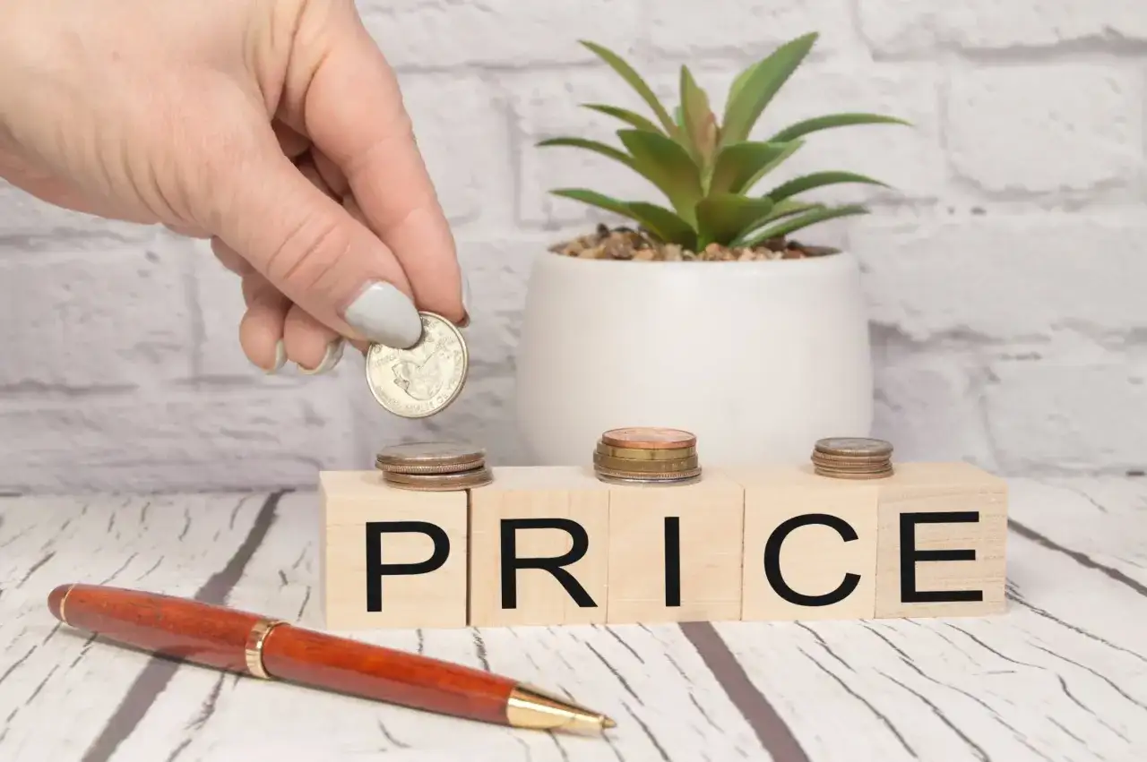 Dłoń kładzie monetę na kostce z literą "P", obok kostek z napisem "RICE". Zastanawiasz się, o ile służebność obniża wartość nieruchomości?
