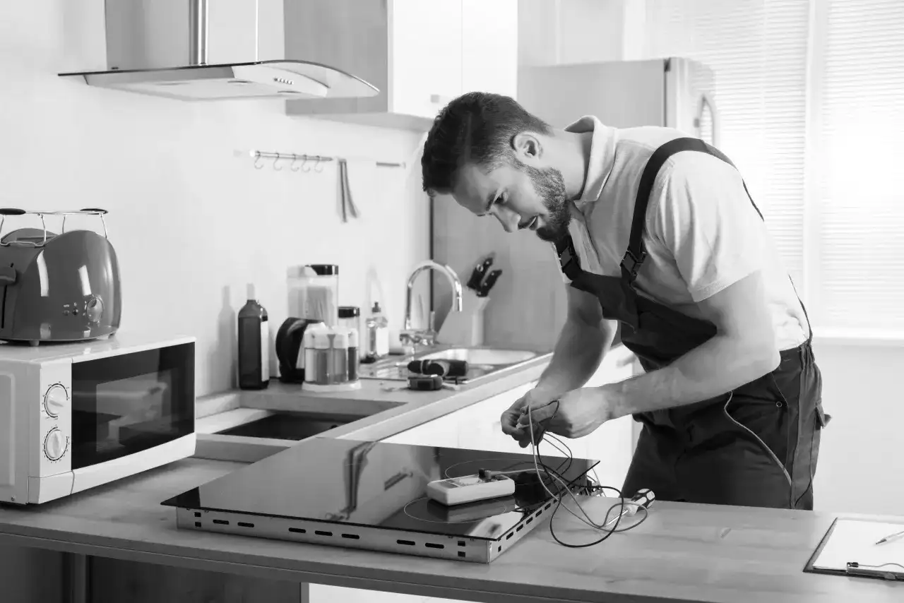 Instalator pracuje nad podłączeniem płyty indukcyjnej, przygotowując się do montażu piekarnika.