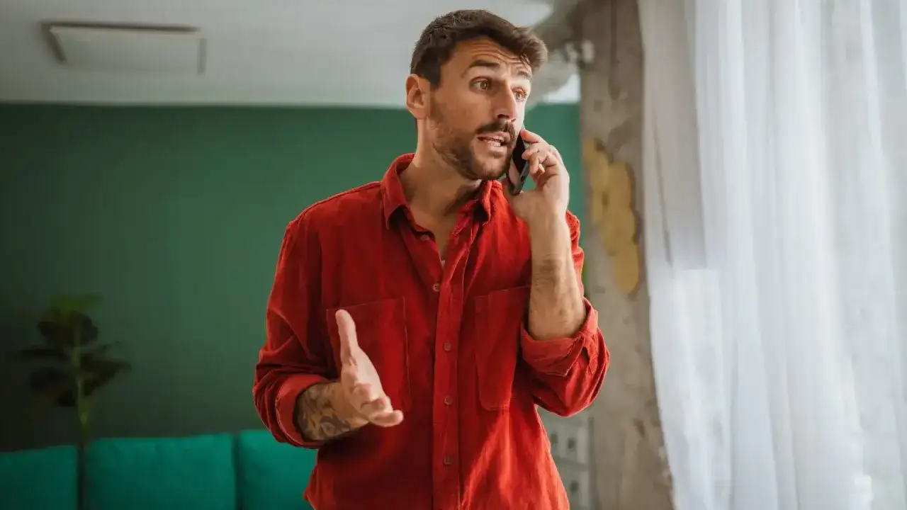 Mężczyzna w czerwonej koszuli rozmawia przez telefon, gestykulując.