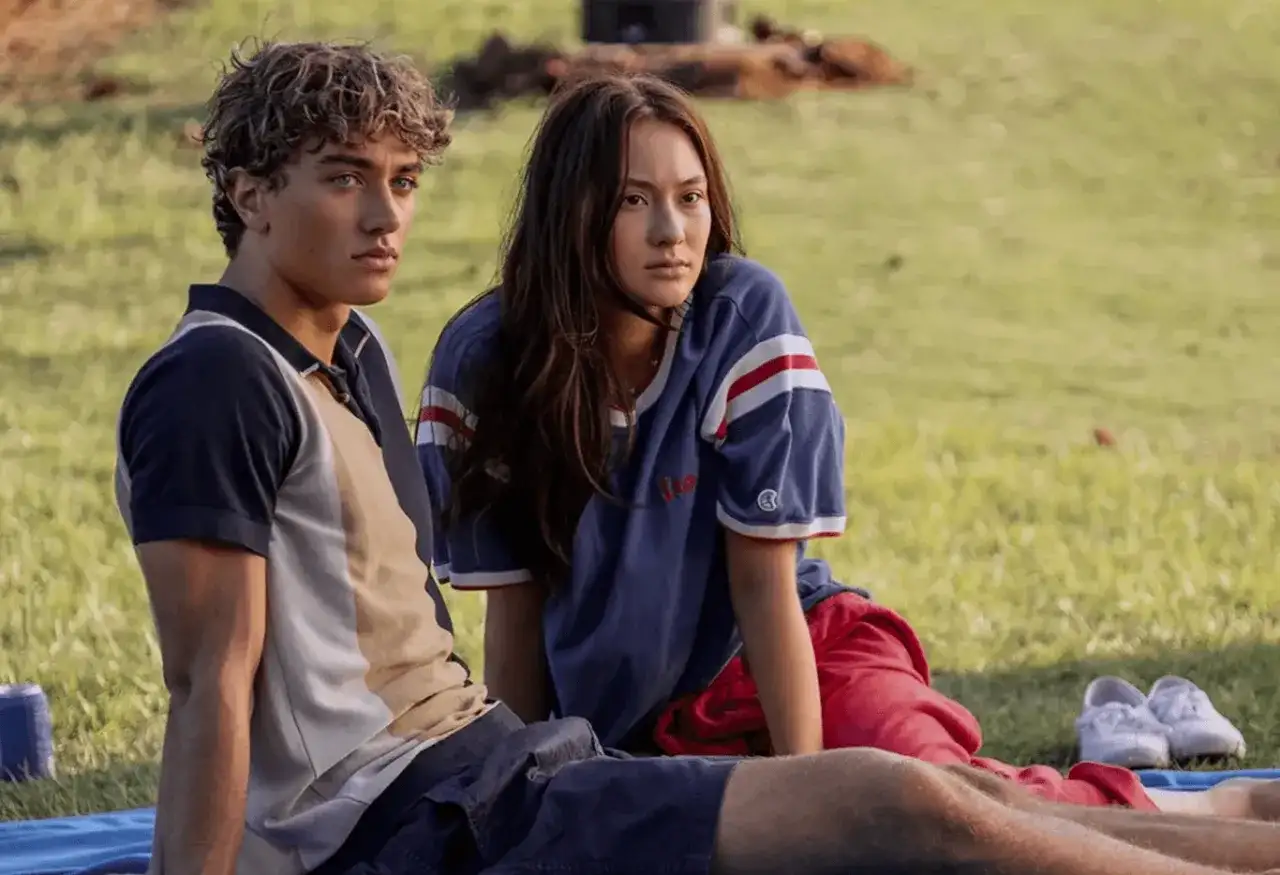 Młodzi ludzie siedzą na trawie. Ona w bluzie z czerwonymi pasami, on w koszulce polo. Czy to początek ich historii, jak w "Tego lata stałam się piękna sezon 3"?