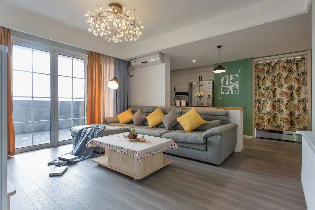 Nowoczesne oświetlenie pokoju tworzy przytulną atmosferę. W centralnym punkcie wisi designerska lampa, a obok niej stojąca lampa rzuca ciepłe światło na szarą sofę.