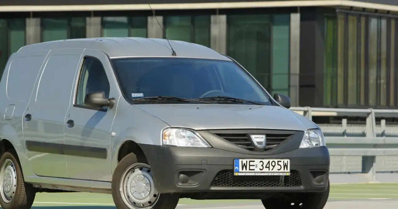 Srebrny Dacia Logan Van z polskimi tablicami WE 3495W zaparkowany przed nowoczesnym budynkiem.