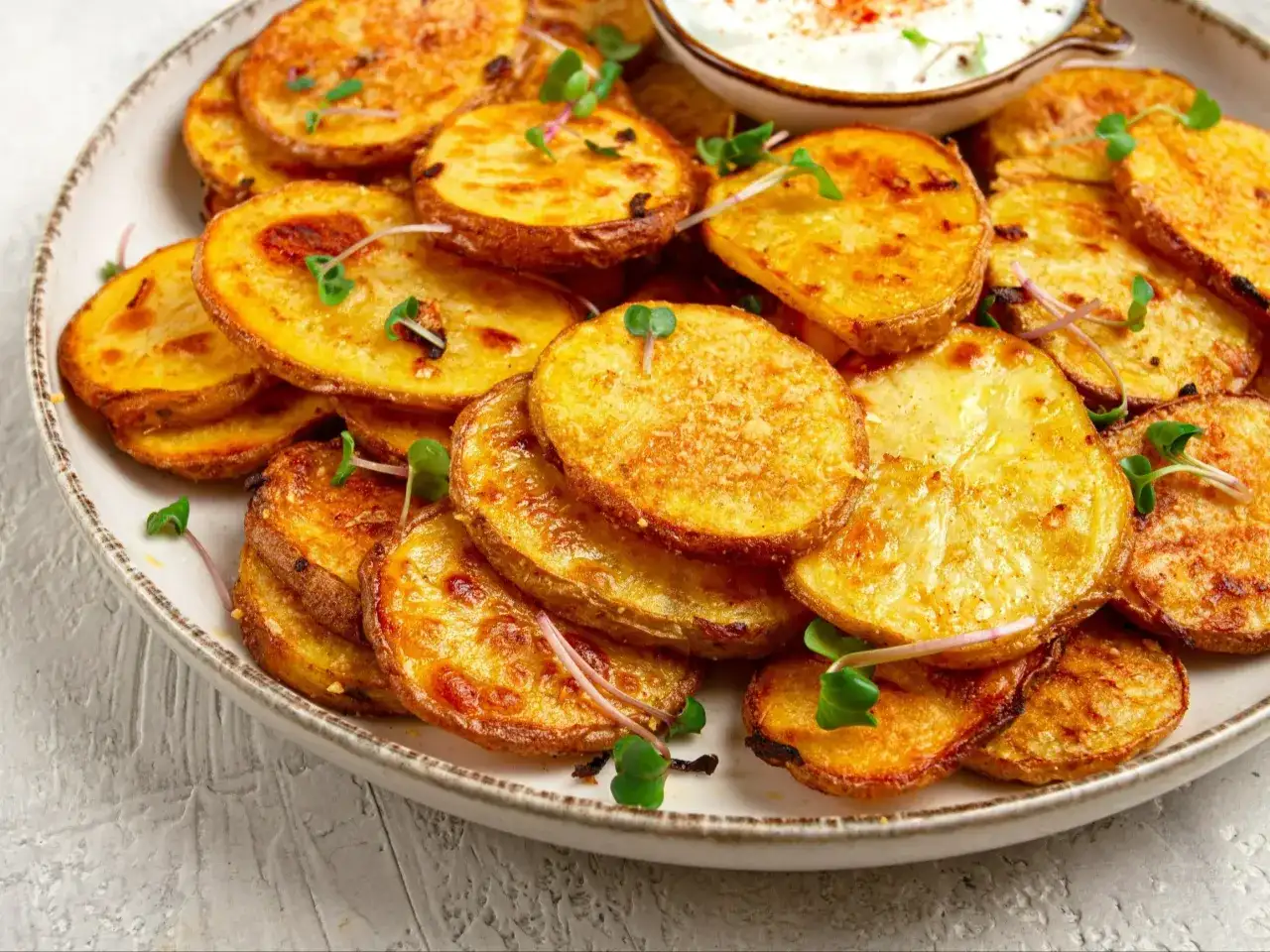 Chrupiące, złociste plasterki ziemniaków z dipem i kiełkami na talerzu.