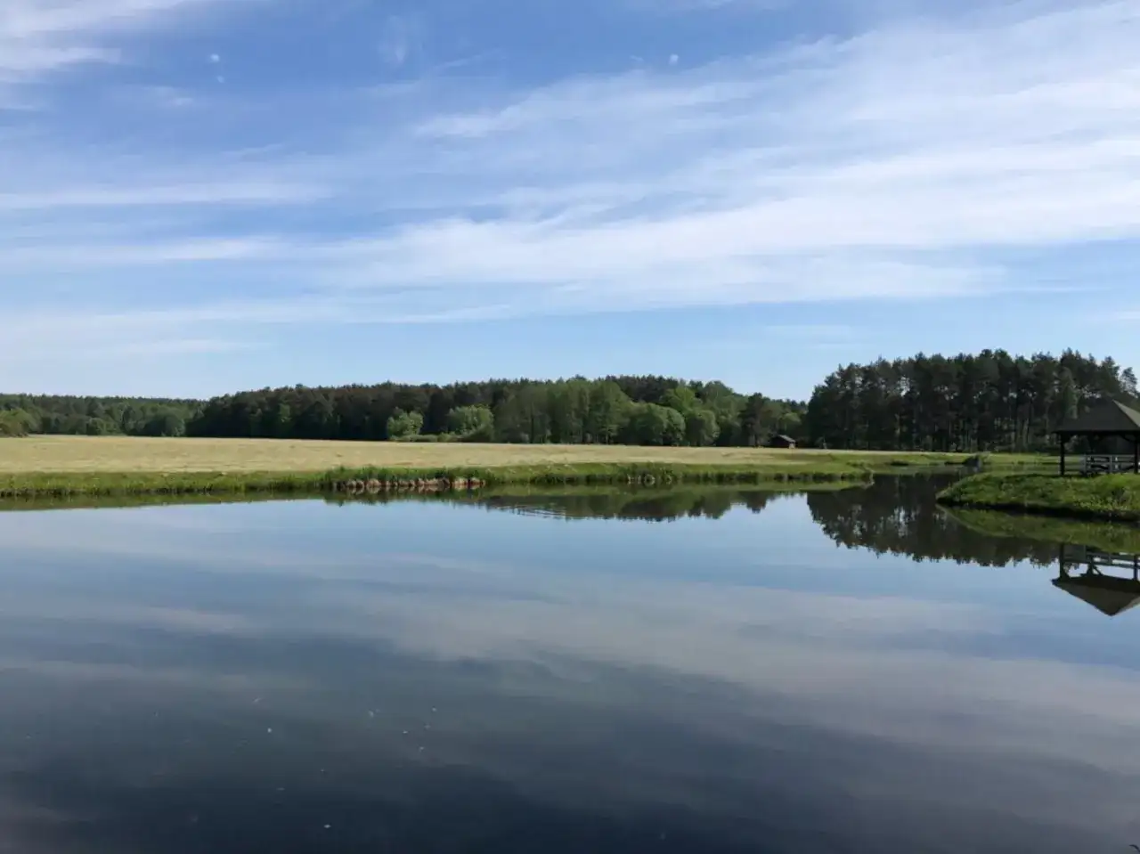 Spokojne jezioro z odbiciem nieba i lasu, z altaną na brzegu.