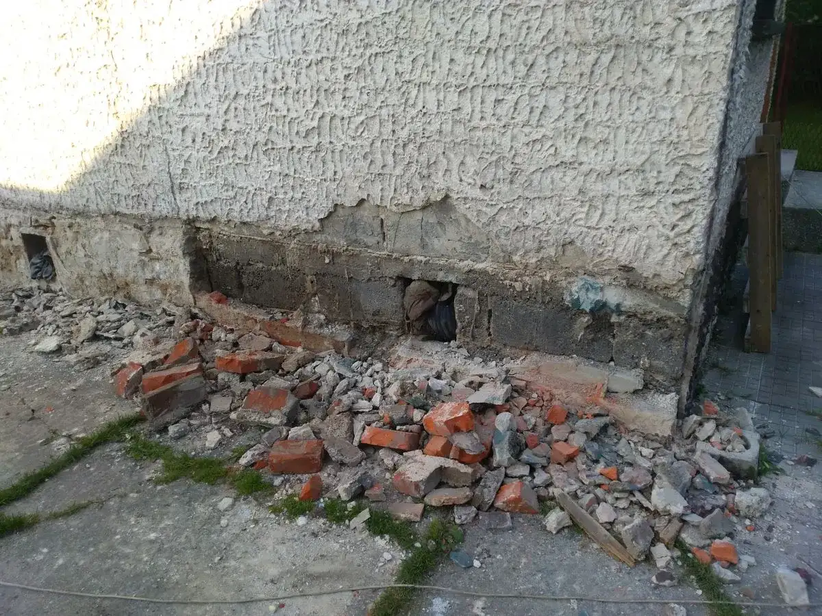 Odkopany fragment ściany z widocznymi uszkodzeniami, gruz i cegły. Rozpoczęcie prac, jak wzmocnić stare fundamenty z kamienia.