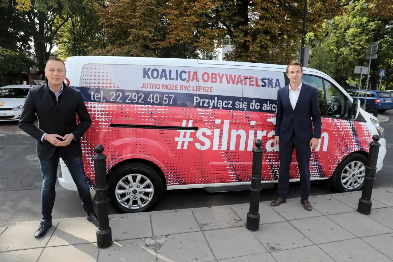 Dwóch mężczyzn stoi obok vana z napisem "Koalicja Obywatelska" i hasłem "#silnirazem".
