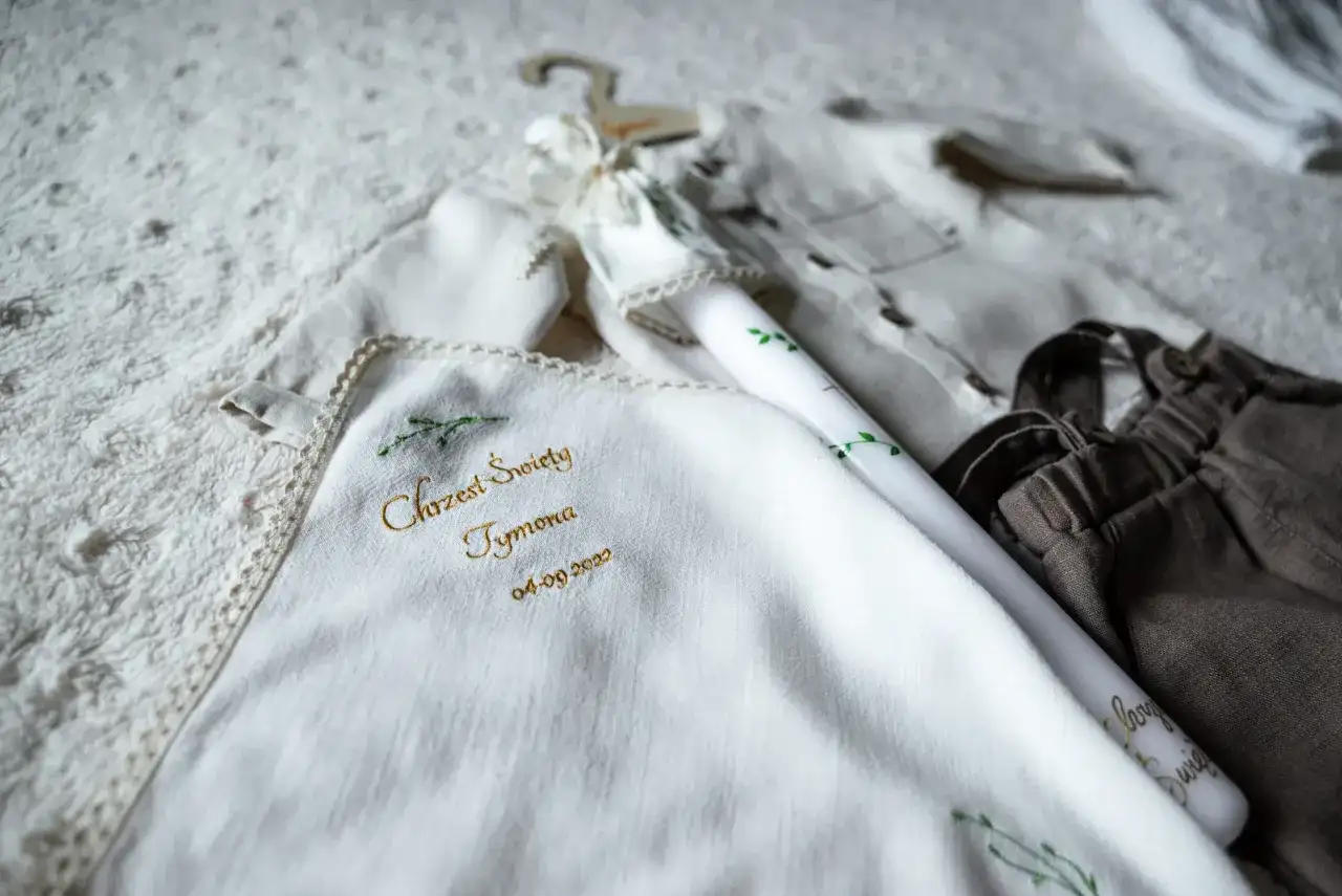 Biała szatka z haftem "Chrzest Święty Tymona" i świeca. Zastanawiasz się, ile bierze fotograf za chrzciny?