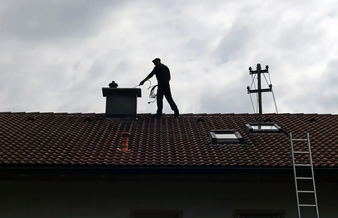 Kominiarz na dachu przygotowuje się do pracy. Zastanawiasz się, ile kosztuje szlamowanie komina?