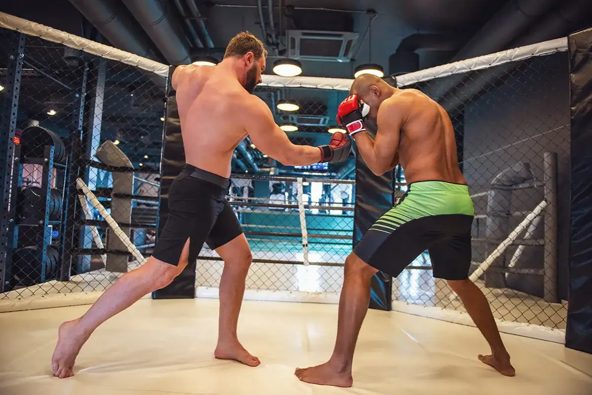 Dwóch mężczyzn walczy w klatce MMA, jeden w rękawicach bokserskich.