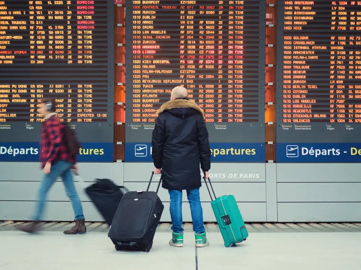 Ludzie z walizkami czekają na lotnisku w Paryżu, patrząc na tablicę odlotów.