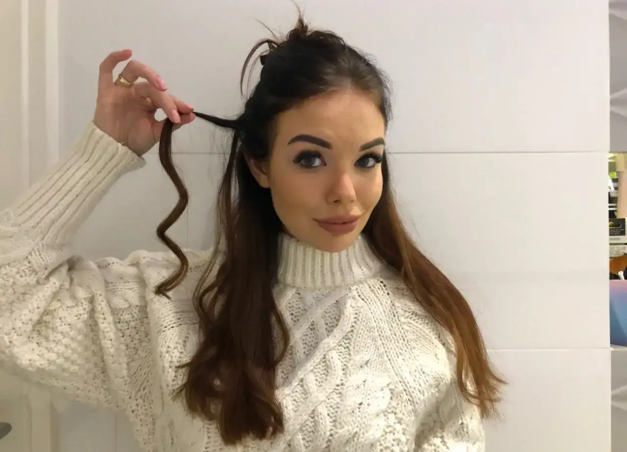 Kobieta w białym swetrze pokazuje lok na włosach.