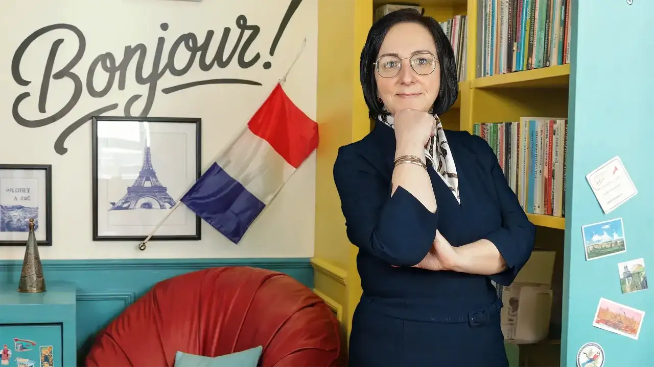 Kobieta w okularach, otoczona francuskimi akcentami, jak "Bonjour!" i flaga. Uczy zaimków wskazujących francuski.