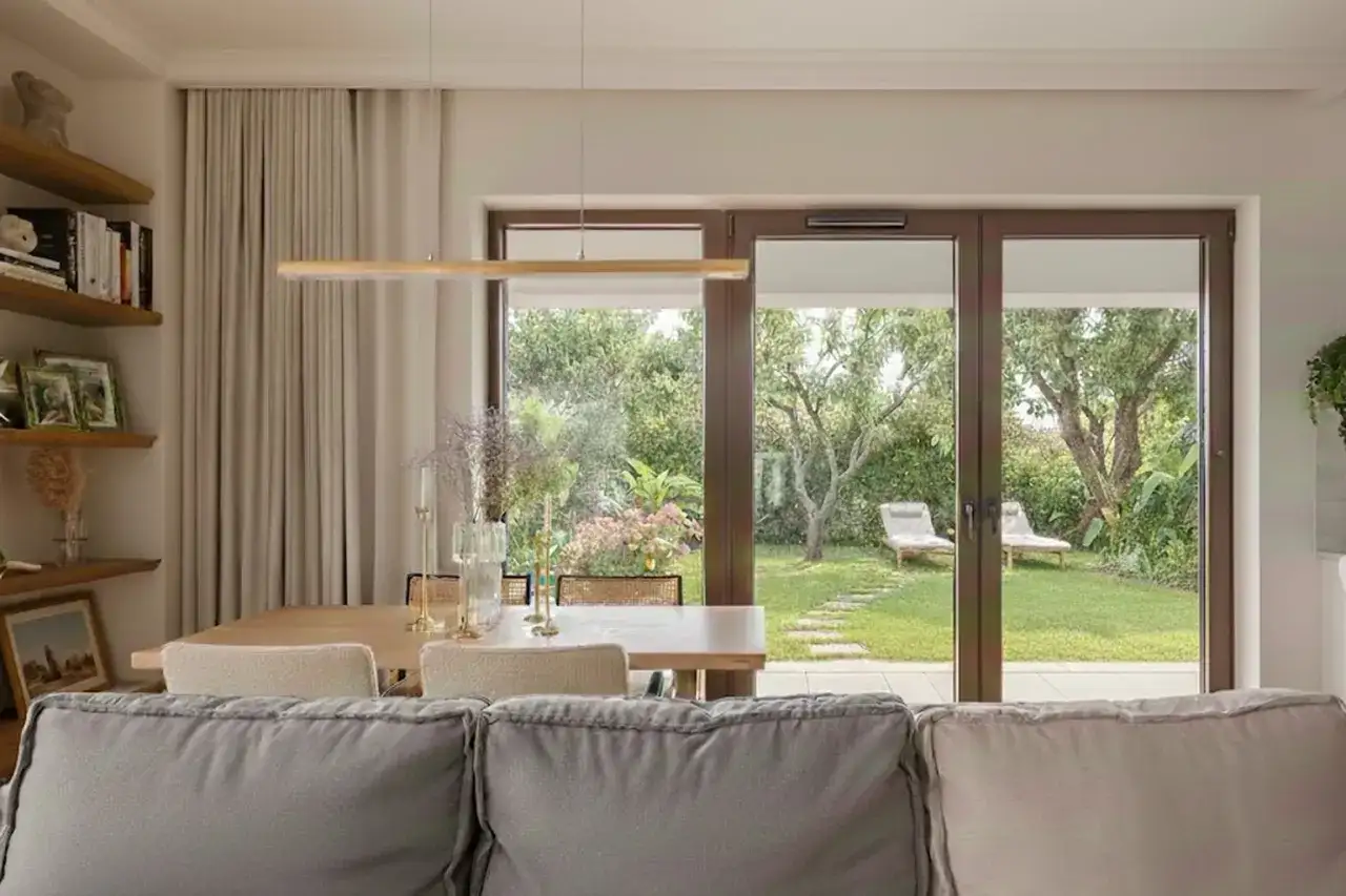 Nowoczesne wnętrze z widokiem na ogród. Zamiast karnisza, zasłony wiszą na szynie ukrytej w suficie, tworząc minimalistyczny efekt.