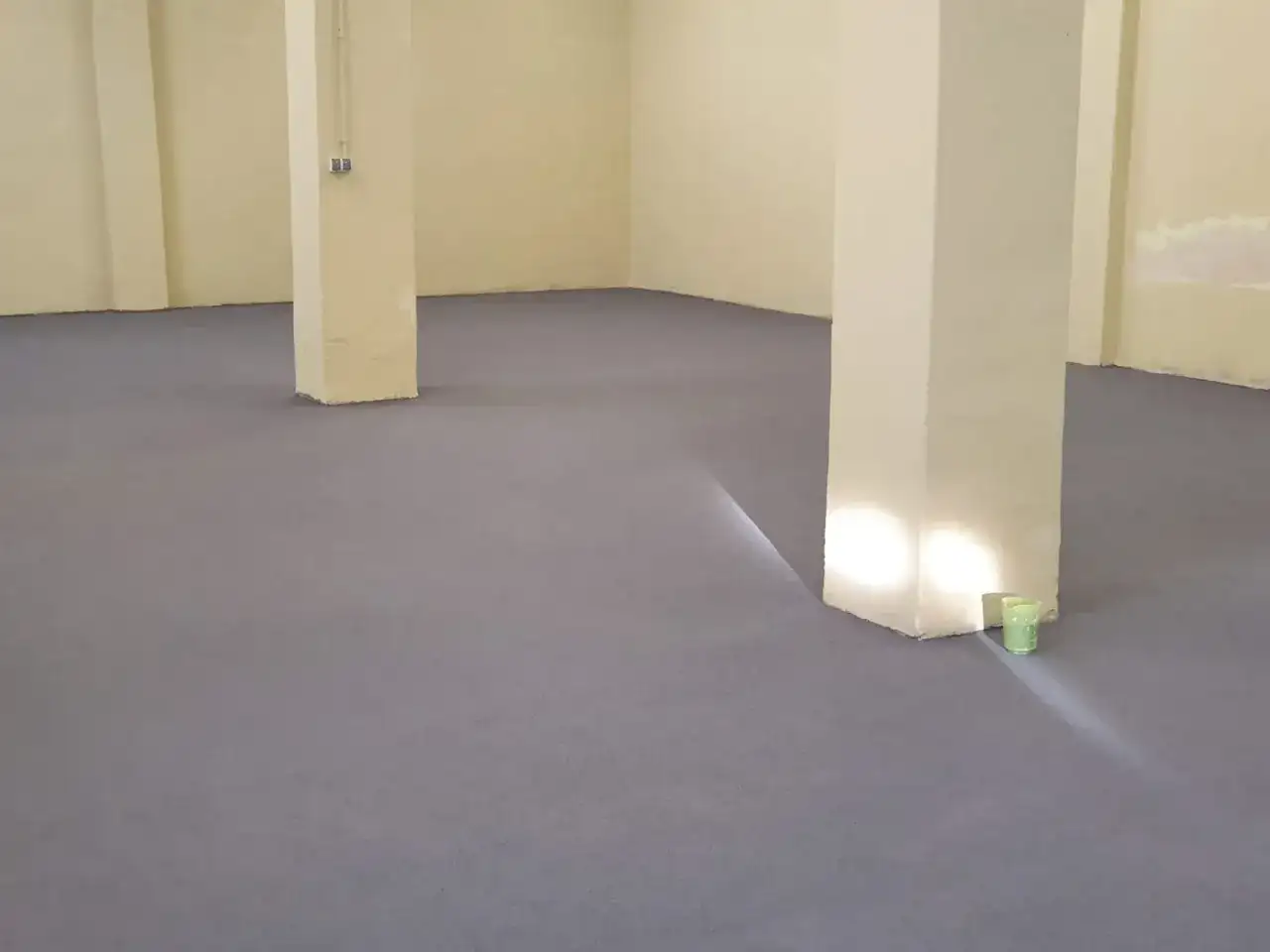 Nowa, szara posadzka betonowa w domu, z jasnymi filarami i żółtymi ścianami.