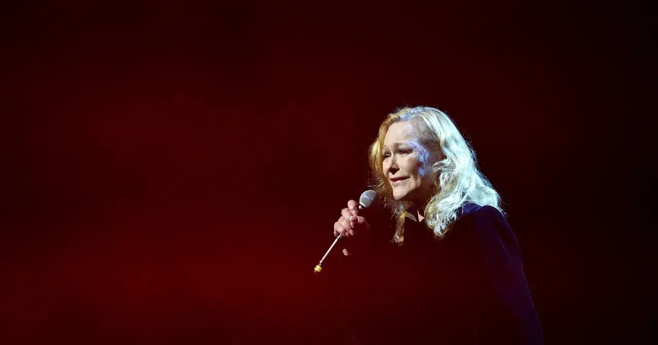 Blondynka śpiewa do mikrofonu, a jej głos niesie ze sobą zapach róży tekst.