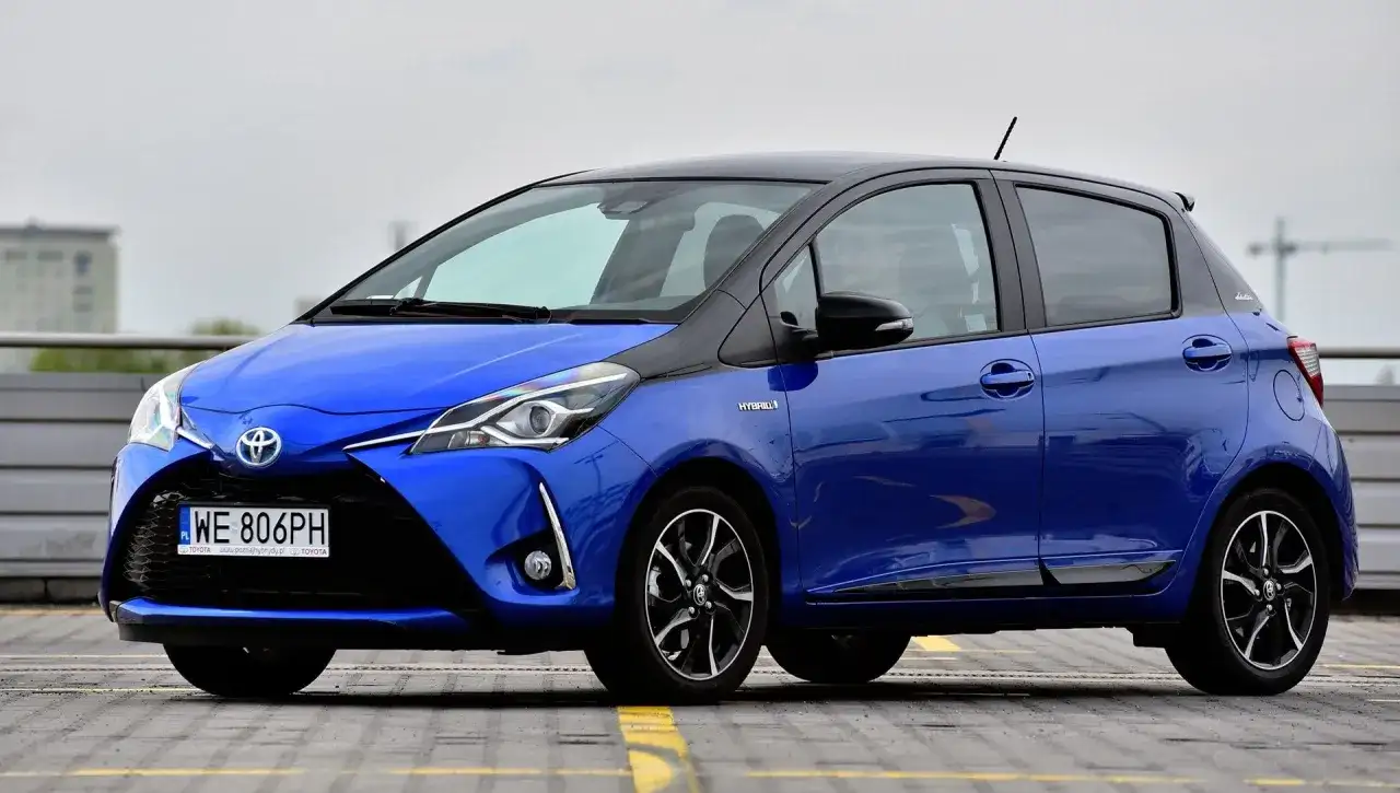 Niebieska Toyota Yaris Hybrid, z czarnym dachem, zaparkowana na zewnątrz. Ile koni ma Toyota Yaris? Ten model ma 100 KM.