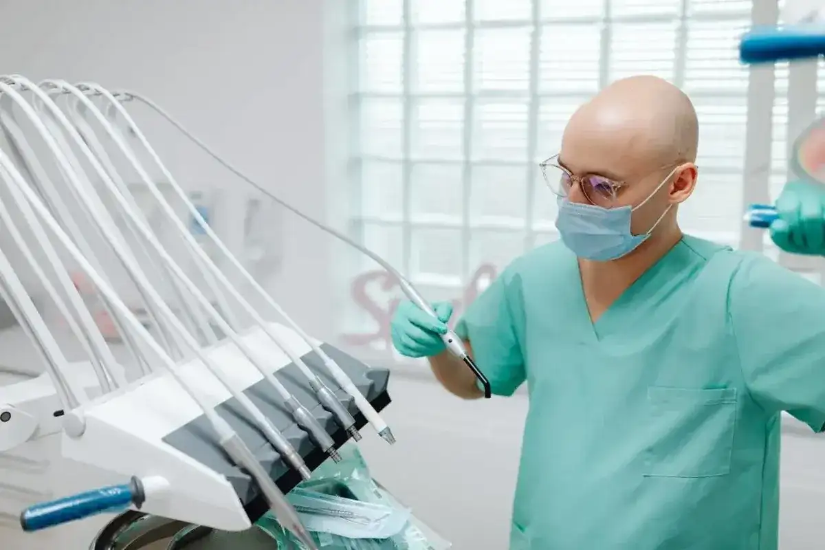 Dentysta w masce i okularach trzymający narzędzie przy unitu stomatologicznego.