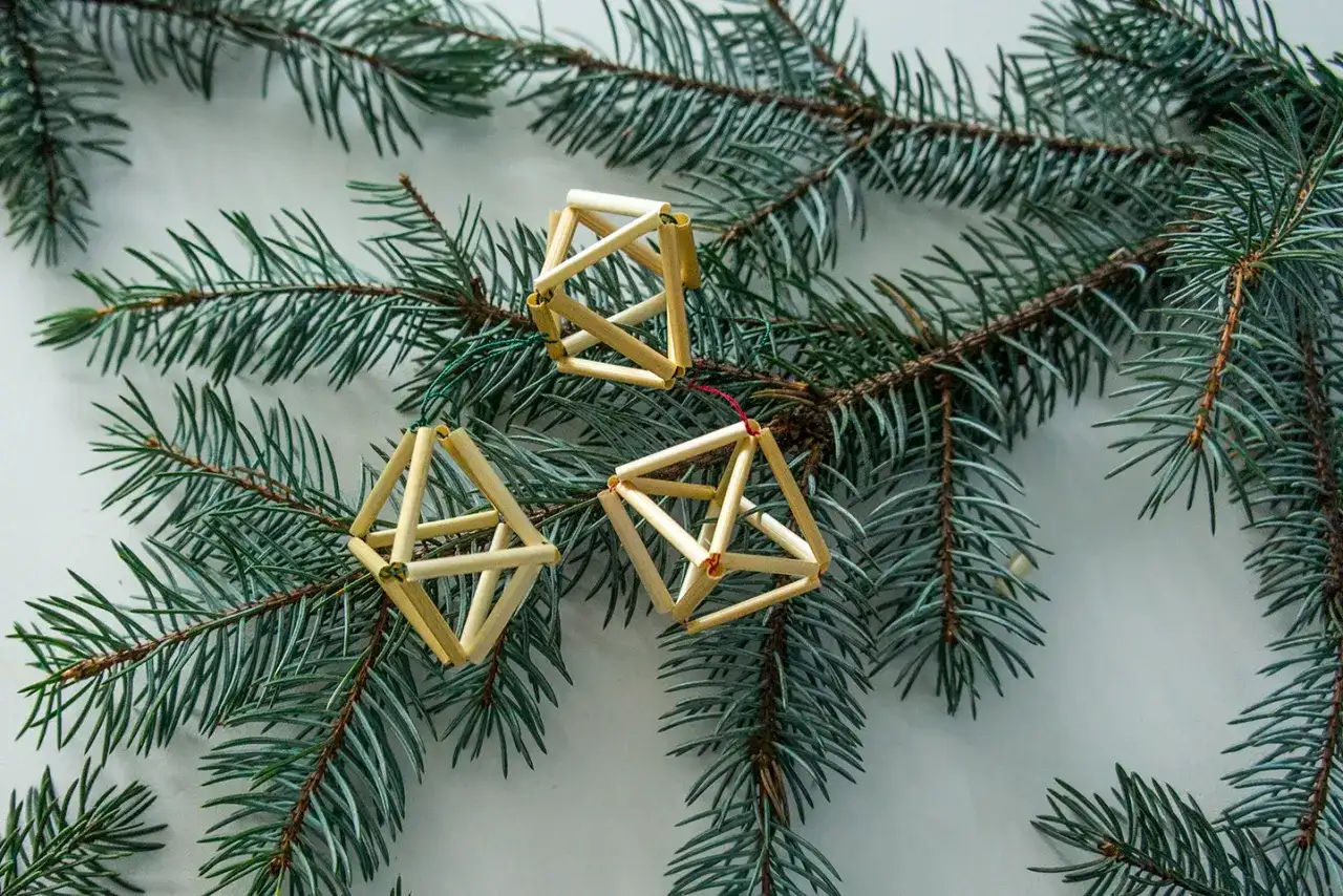 Trzy ozdoby choinkowe ze słomy w kształcie brył geometrycznych wiszą na gałęzi świerku.