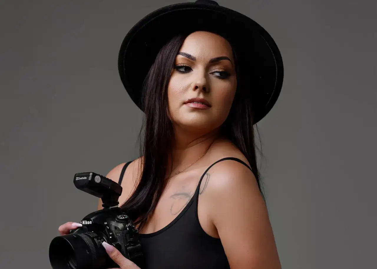 Kobieta w czarnym kapeluszu trzyma aparat fotograficzny Nikon, patrząc w bok.