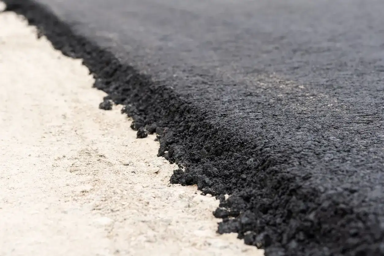 Zbliżenie na świeżo położony asfalt na jasnym podłożu.