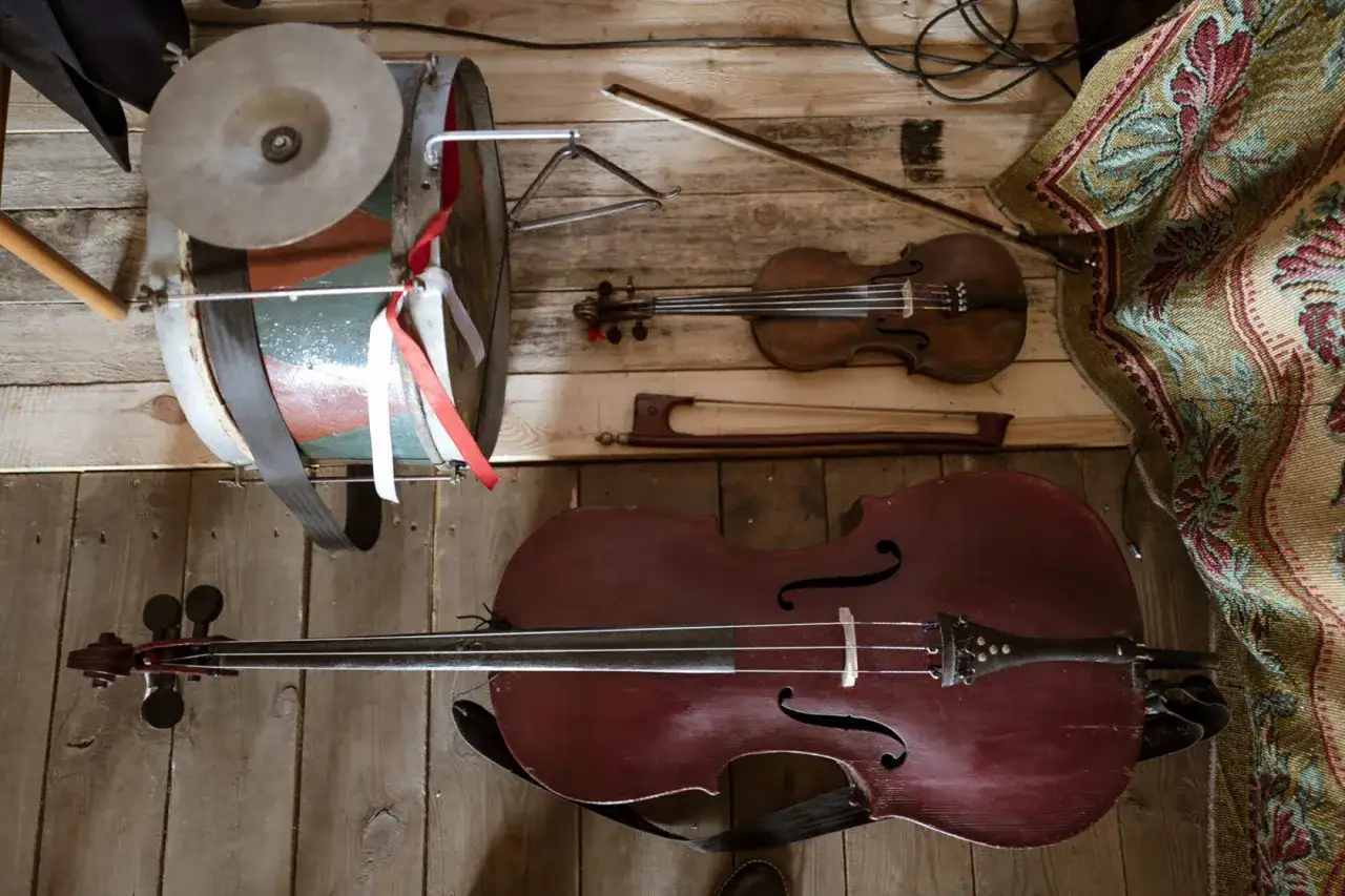 Instrument ludowy podobny do wiolonczeli, skrzypce i bębenek leżą na drewnianej podłodze.