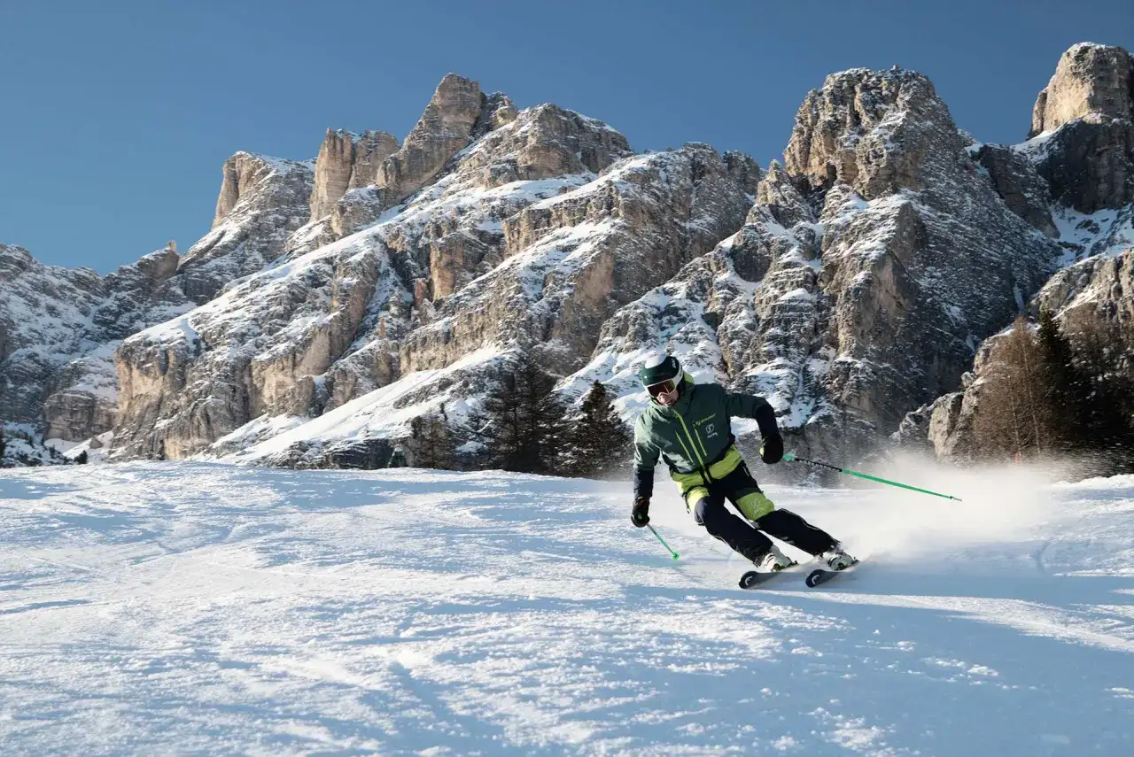 Narciarz szusuje po ośnieżonym stoku, w tle majestatyczne góry Alpy.