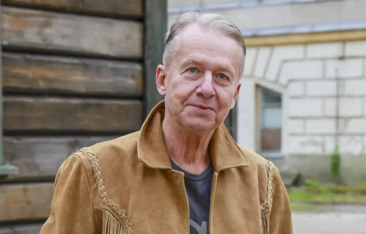 Bogusław Linda w brązowej kurtce z zamszu, z frędzlami i ozdobnymi szwami.