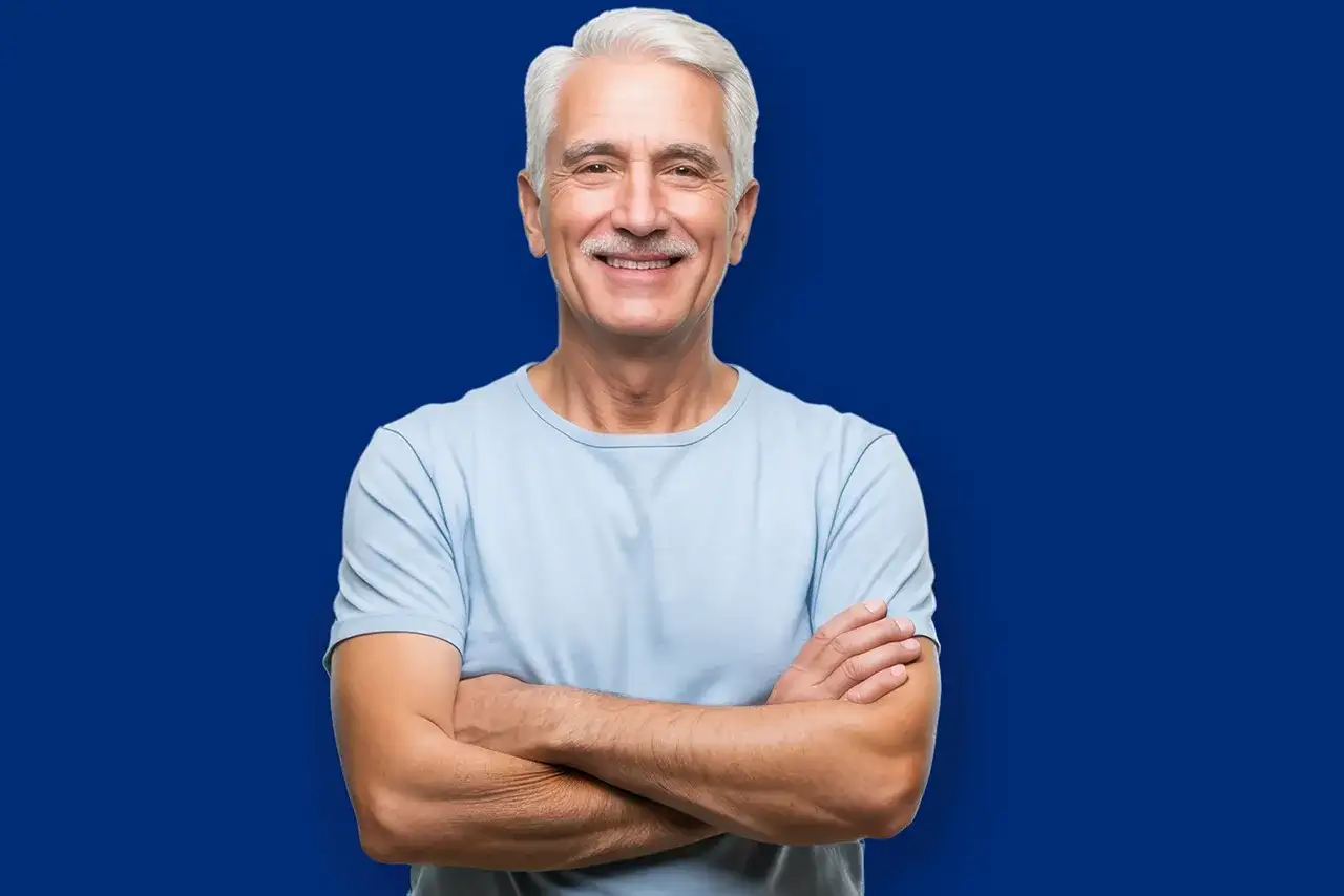 Uśmiechnięty starszy mężczyzna z siwymi włosami i wąsami, w jasnoniebieskiej koszulce, z rękami skrzyżowanymi na piersi. Wygląda jak żywy dowód na to, że wiek to tylko liczba, efekt Galatei w czystej postaci.