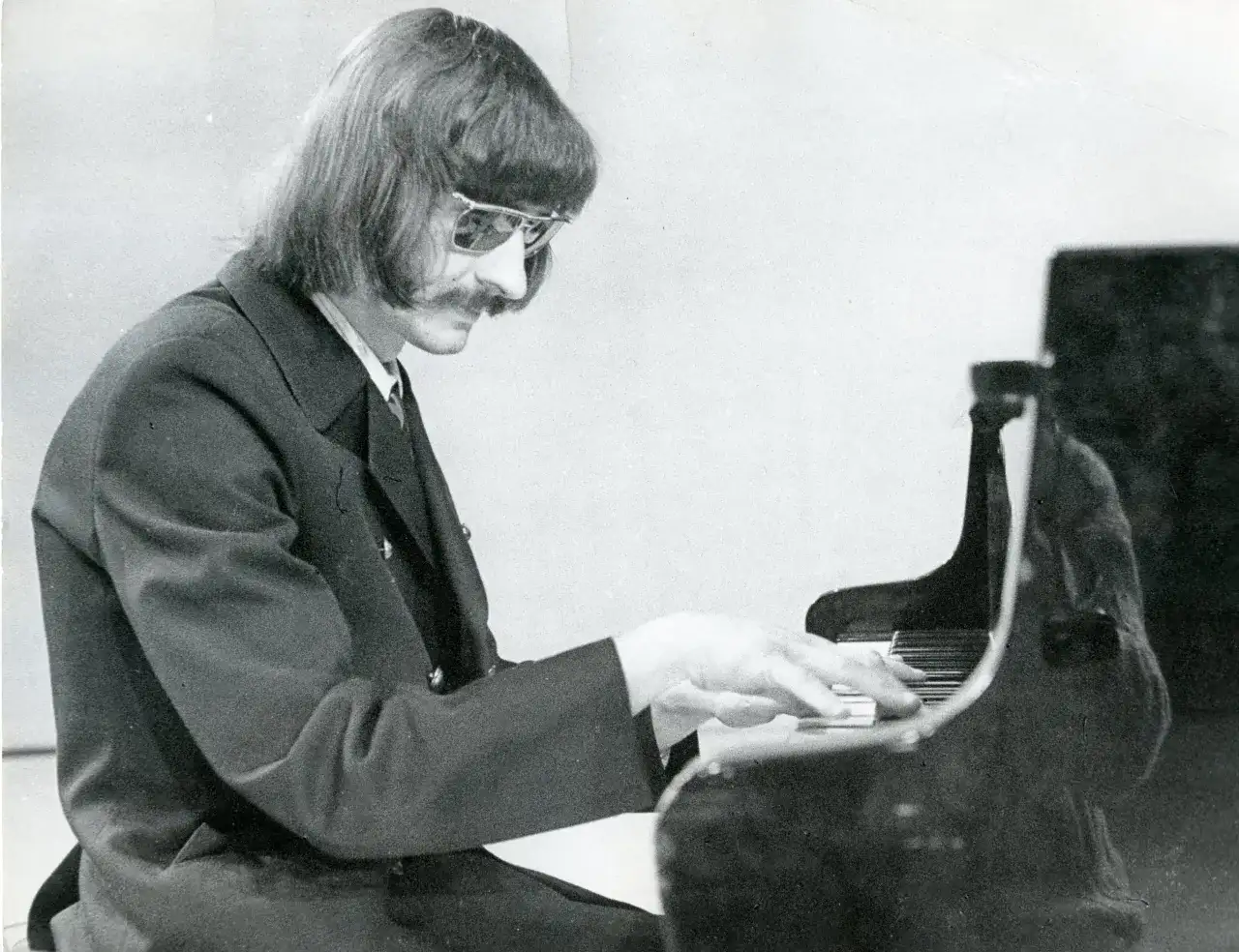 Mieczysław Kosz w okularach i garniturze gra na fortepianie.