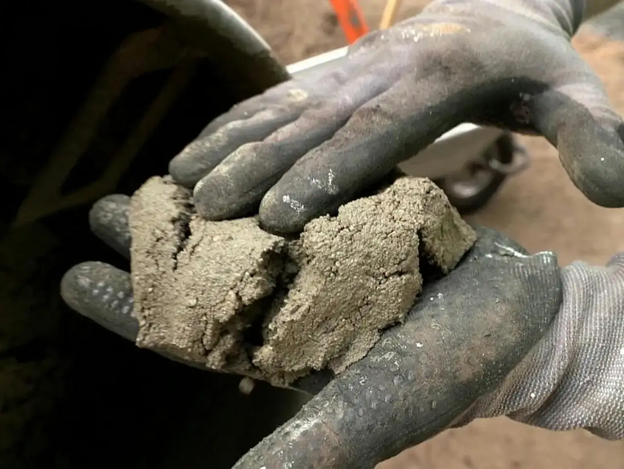 Rękawice robocze trzymają grudki zaschniętego betonu, co jest pierwszym krokiem w procesie, jak wyczyścić betoniarkę.