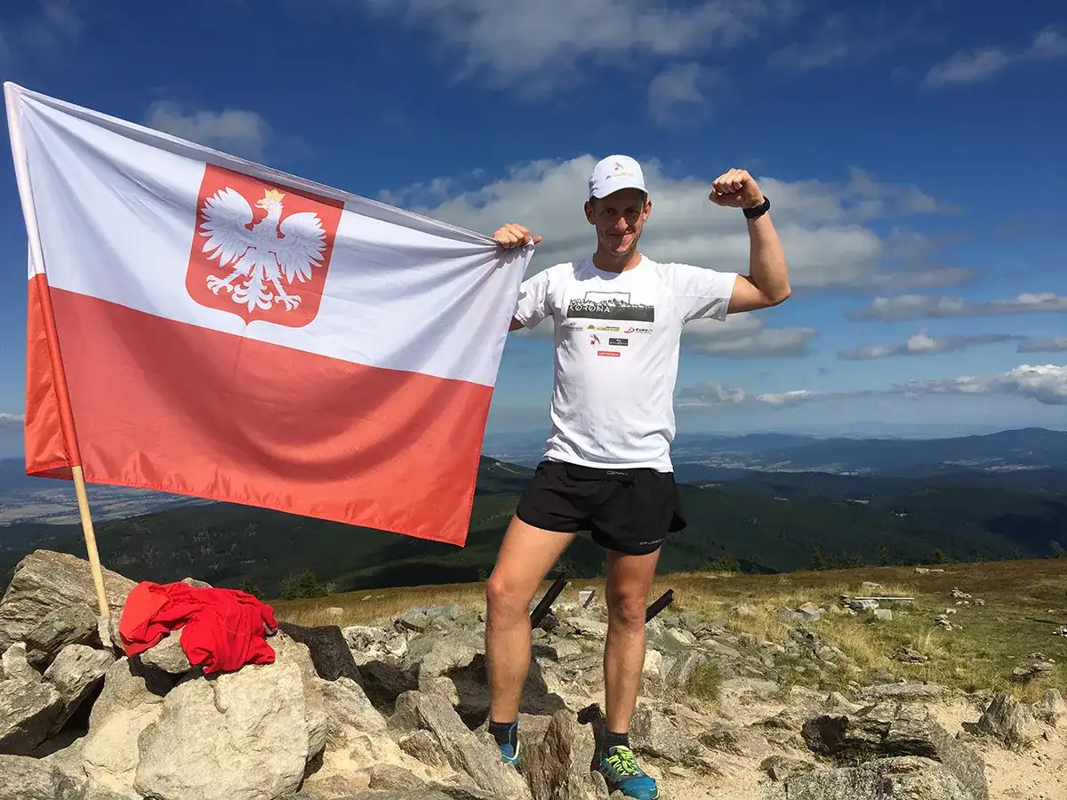 Mężczyzna na szczycie górskim z polską flagą, zdobywca diadem gór polskich.