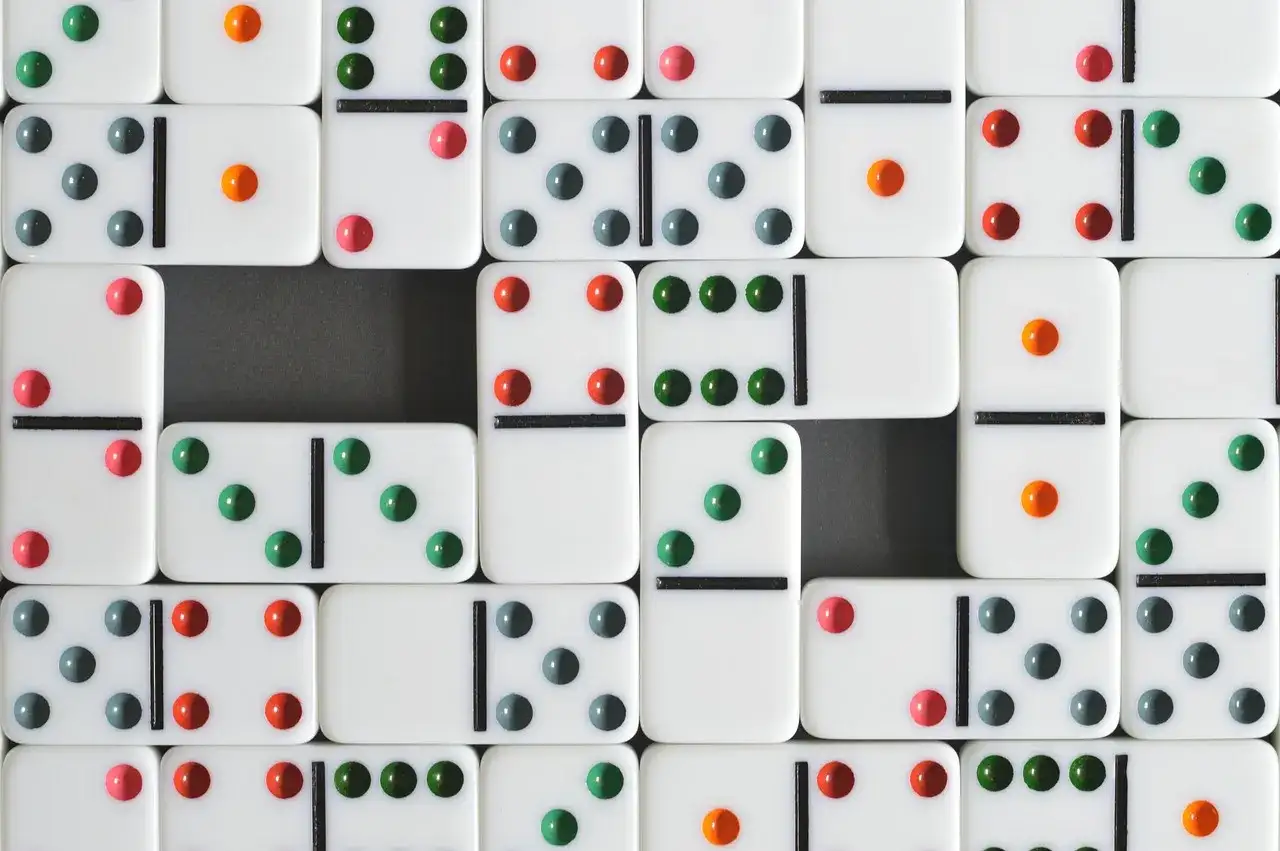 Wiele białych kostek domino z kolorowymi kropkami, tworzących wzór. Ile kostek domino?