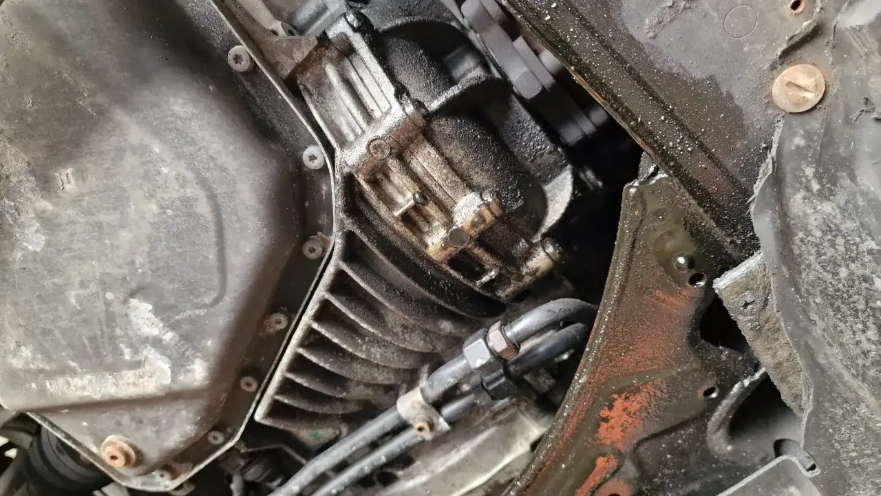 Widok od spodu na skrzynię korbową silnika spalinowego, z widocznymi przewodami i elementami mocowania.