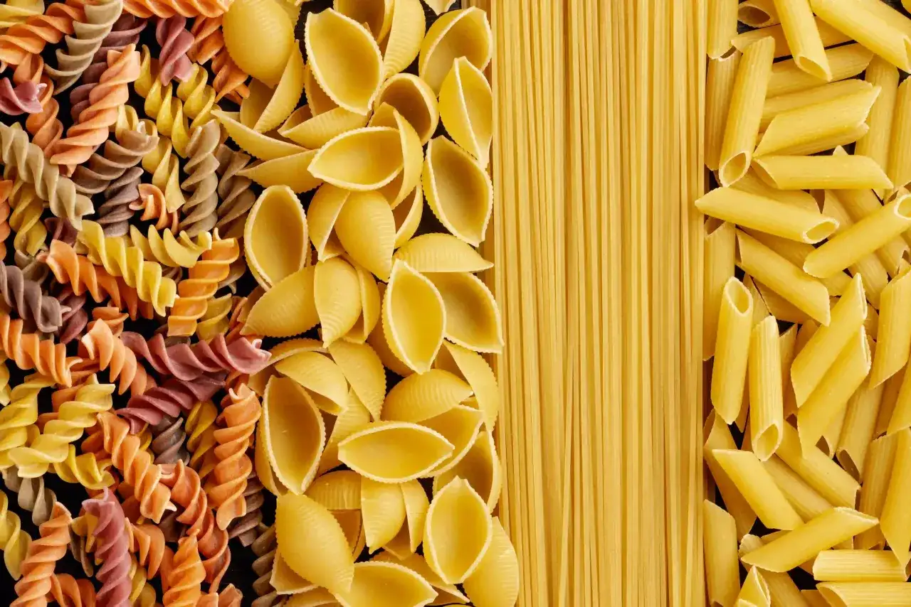 Różne rodzaje makaronu: kolorowe fusilli, muszelki, spaghetti i penne. Wybór wpływa na indeks glikemiczny posiłku.