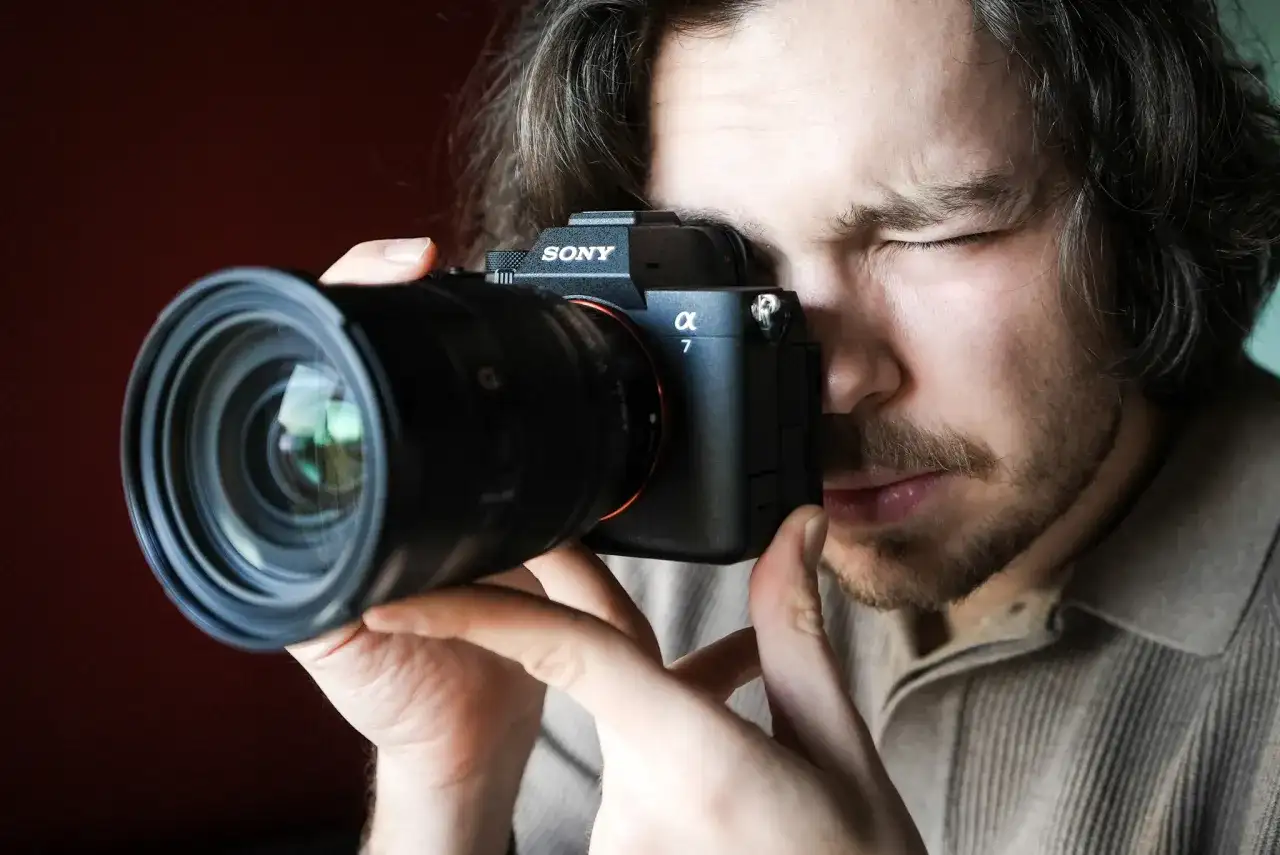 Mężczyzna zamyka oko, patrząc przez wizjer aparatu Sony Alpha 7. Premiera Sony a7 IV budzi emocje.