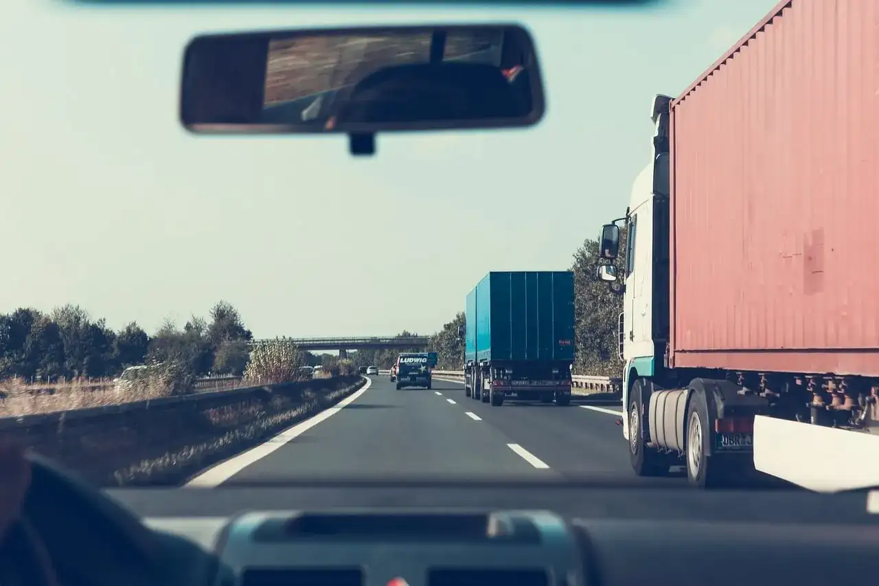 Widok z kabiny samochodu na autostradzie z ciężarówkami i innymi pojazdami.