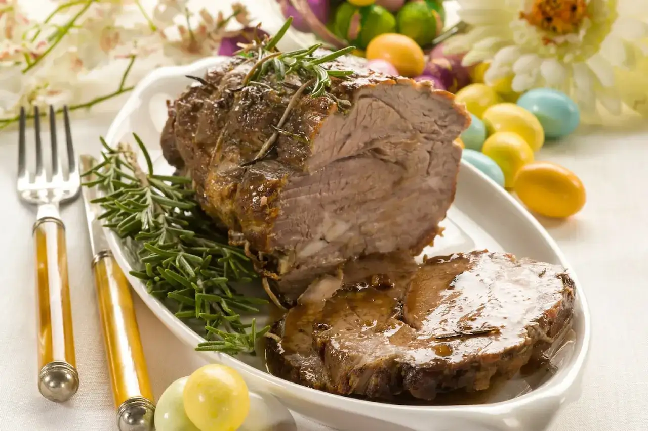 Pyszne pieczone mięso z rozmarynem, idealne jako co na obiad na Wielkanoc. Kolorowe jajka i kwiaty dodają świątecznego klimatu.