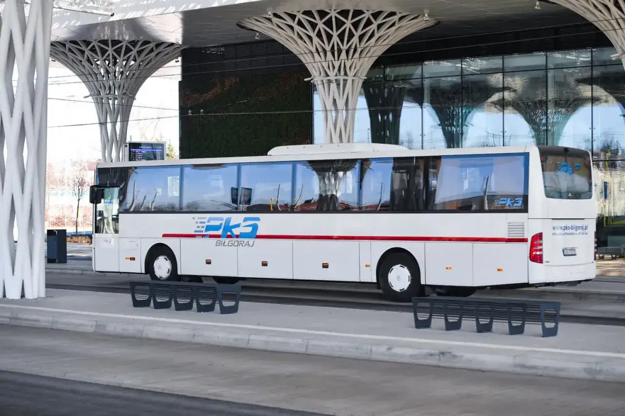 Biały autobus PKS Biłgoraj na nowoczesnym dworcu autobusowym z zieloną ścianą i futurystycznym zadaszeniem.