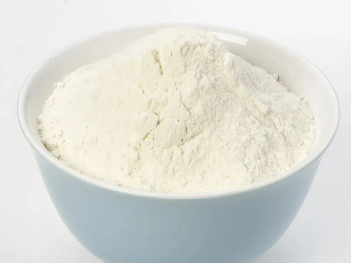 Jasnoniebieska miska wypełniona białym proszkiem, przypominającym mąkę lub cukier puder.