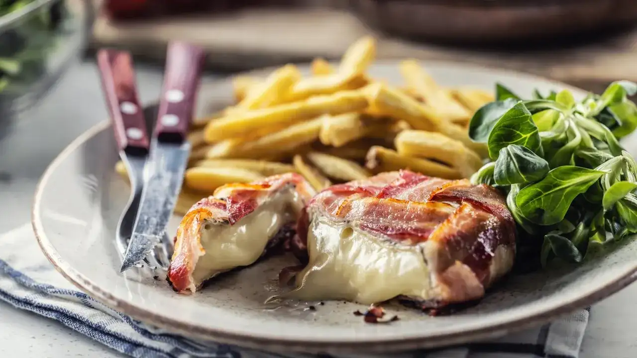 Ser camembert zawinięty w bekon, podany z frytkami i sałatką.