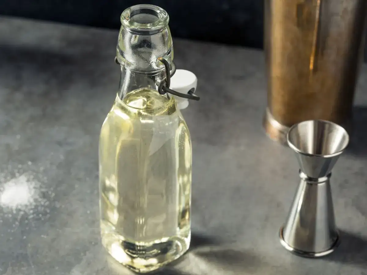 Domowy syrop cukrowy (simple syrup) w butelce, obok jigger i shakera. Idealny do drinków, łatwy do przygotowania krok po kroku.