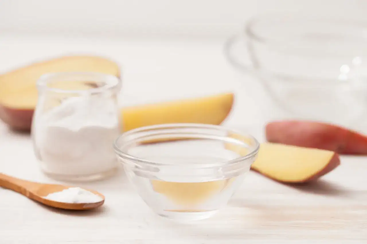 Mąka ziemniaczana w słoiku, woda w miseczce, drewniana łyżka z mąką i kawałki ziemniaków.