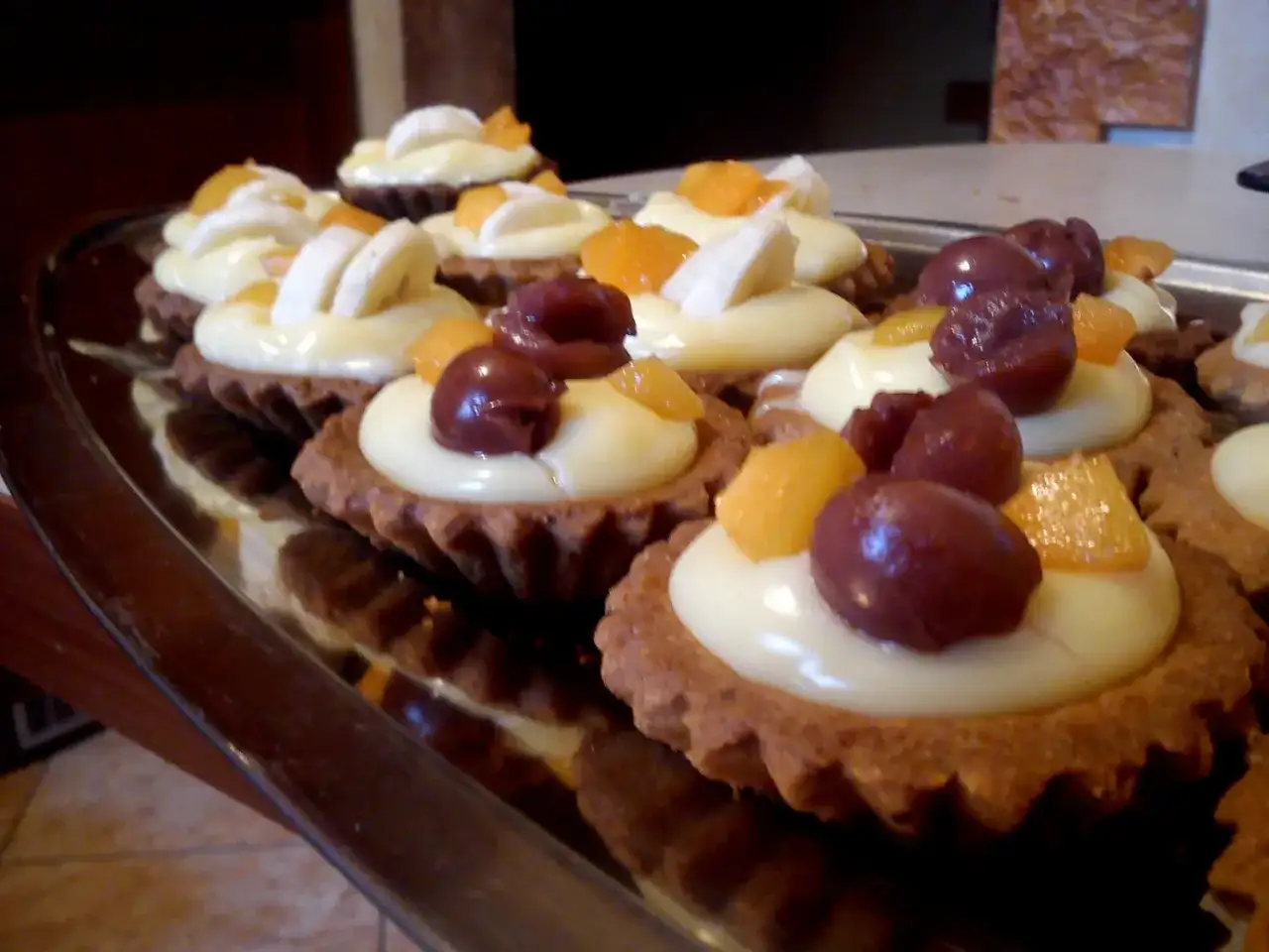 Babeczki z kremem, owocami i wiśniami na tacy.