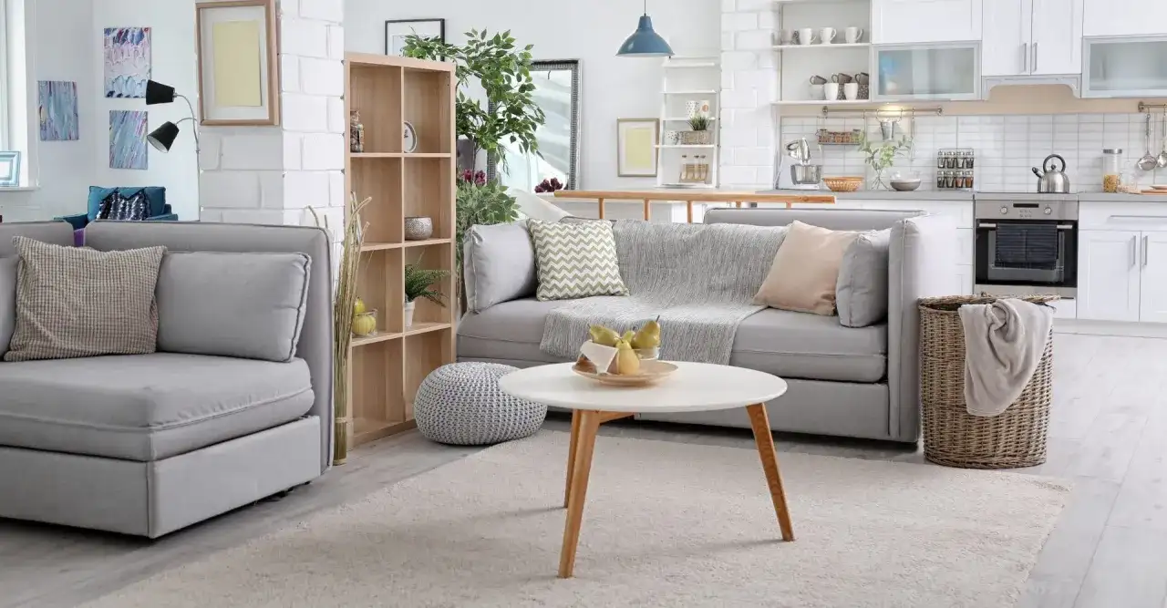 Nowoczesny salon z aneksem kuchennym. Miękka sofa, stolik kawowy z owocami i kosz na pranie. To wszystko warto objąć ubezpieczeniem mienia.