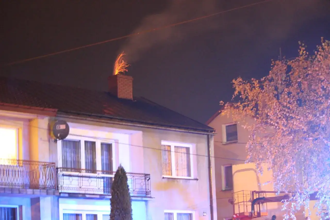 Jasne iskry z komina, czy to normalne? Dym i ogień wydobywają się z ceglanego komina na dachu domu nocą.