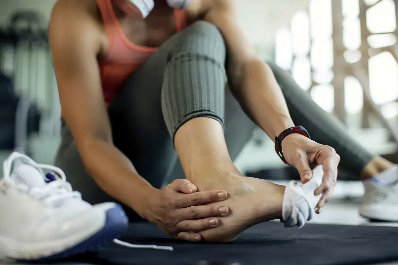 Kobieta w siłowni masuje stopę, czując mrowienie w stopach od kręgosłupa.