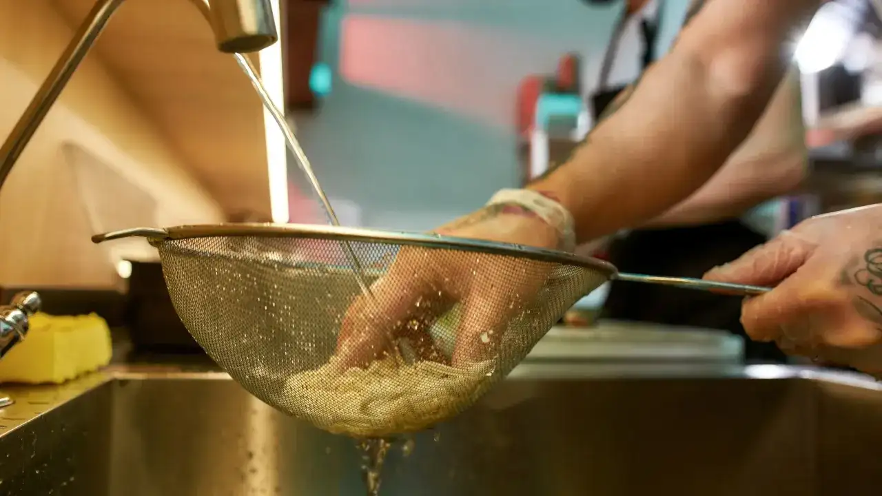 Ręce w rękawiczkach płuczą makaron pod bieżącą wodą, by zapobiec jego sklejaniu.