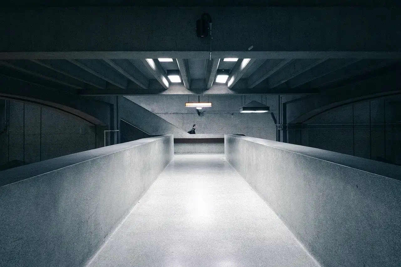 Minimalistyczna przestrzeń z betonowymi ścianami i podłogą. W oddali widać pojedynczą postać. Klasy ekspozycji betonu podkreślają surowość architektury.